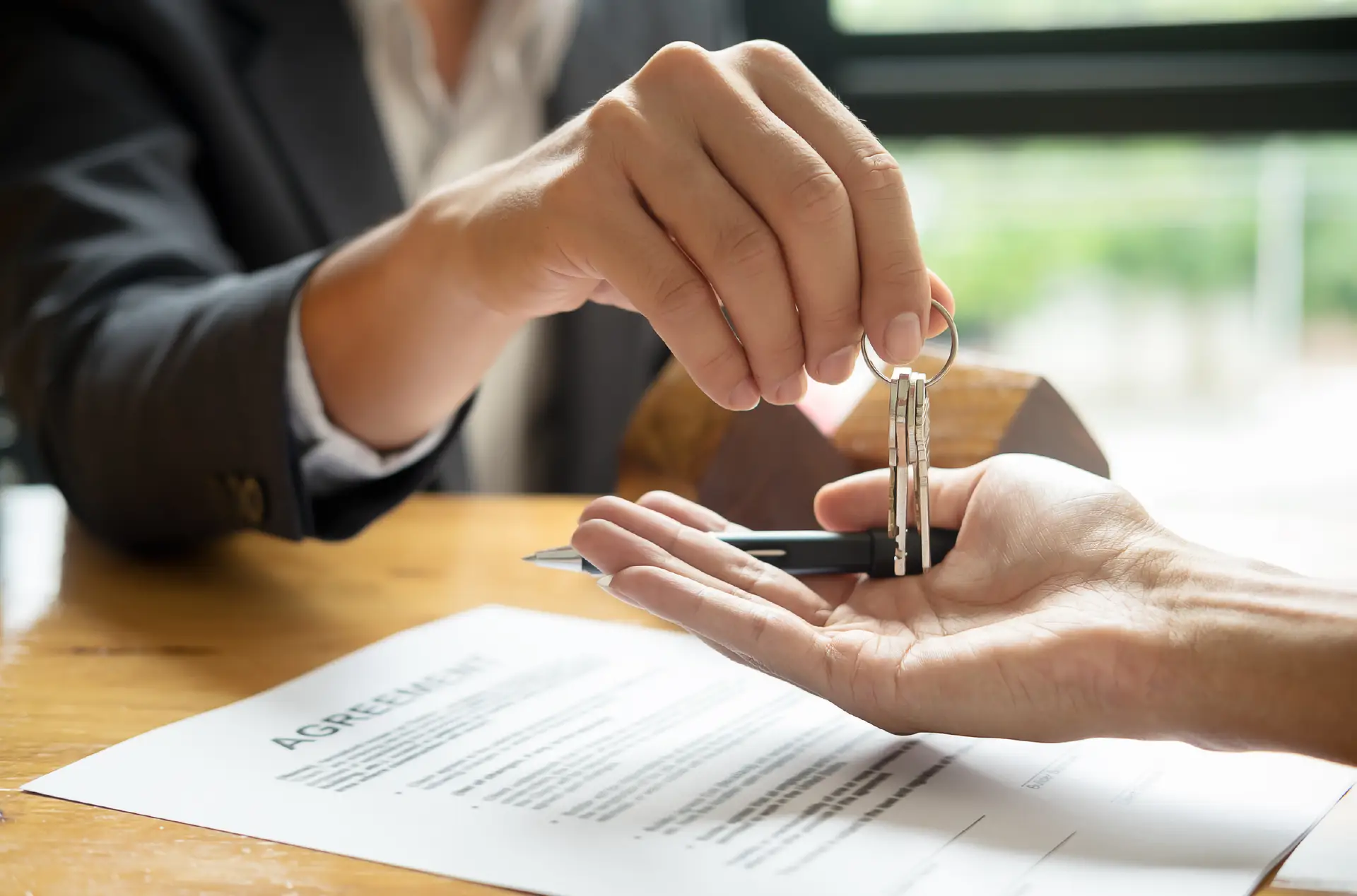 Hands passing house keys across a table at a real estate closing